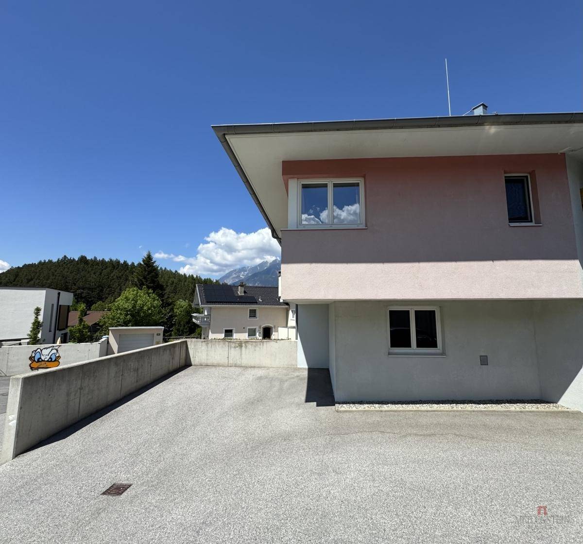 Rückansicht eines modernen Gebäudes mit Parkplatz und Bergblick im Hintergrund.