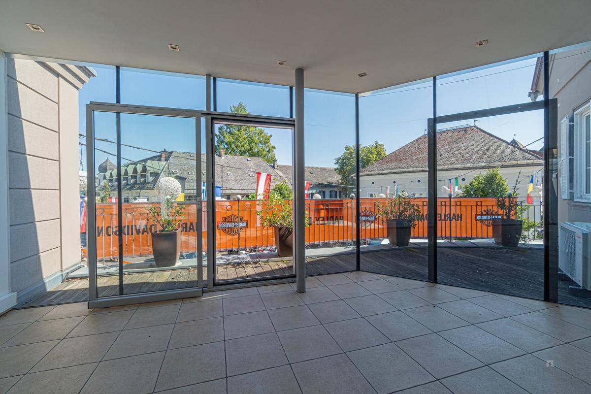 Offener Raum mit Fliesenboden und weitem Blick auf eine Terrasse mit Pflanzen und umliegende Gebäude.