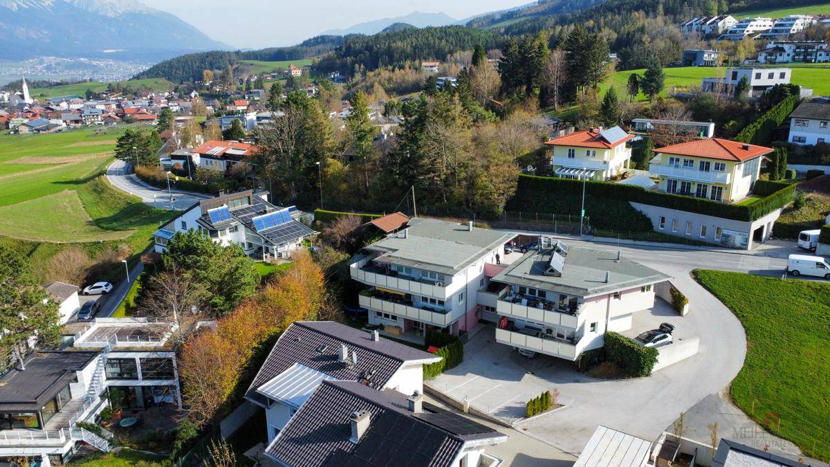Luftaufnahme einer Wohnsiedlung mit mehreren Gebäuden und weitem Blick über die Landschaft und Berge.