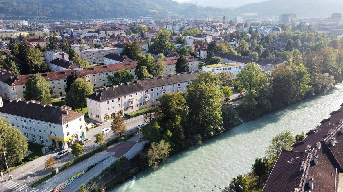 Weitläufige Luftaufnahme der Stadt mit Fluss, Wohngebieten und majestätischen Bergen im Hintergrund.