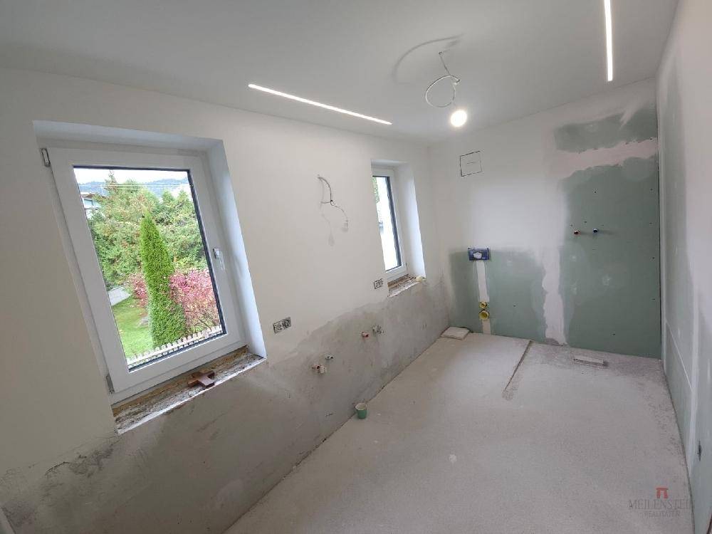 Geräumiges Badezimmer im Rohbau mit zwei Fenstern und moderner Deckenbeleuchtung.