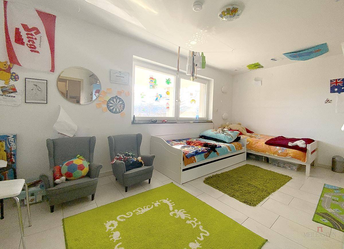 Helles Kinderzimmer mit zwei Betten, bunten Teppichen und spielerischer Dekoration.