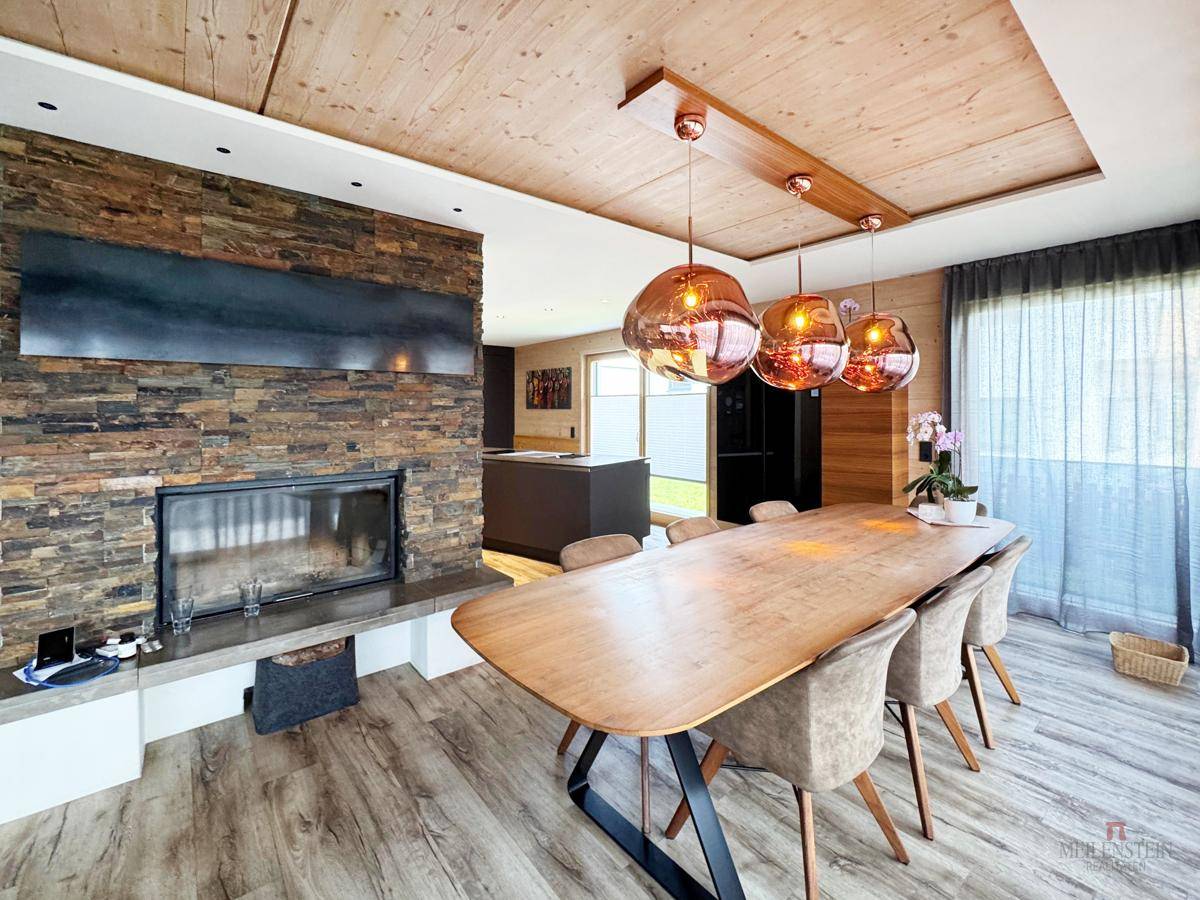 Gemütlicher Essbereich mit Holztisch, modernen Pendelleuchten und Kamin mit Steinverkleidung.