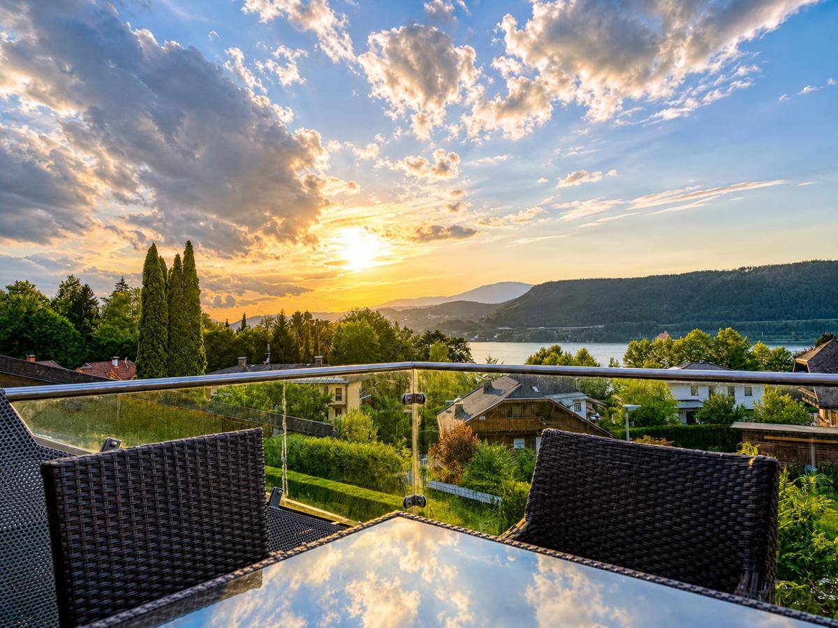 Terrasse mit Glasgeländer und Rattanmöbeln, bietet einen weiten Blick auf den See und die Berge.
