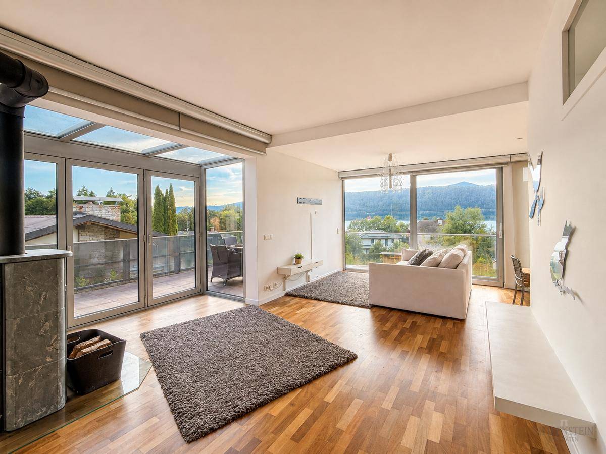 Geräumiges Wohnzimmer mit Holzboden, Kaminofen und Zugang zu einer verglasten Terrasse mit Seeblick.