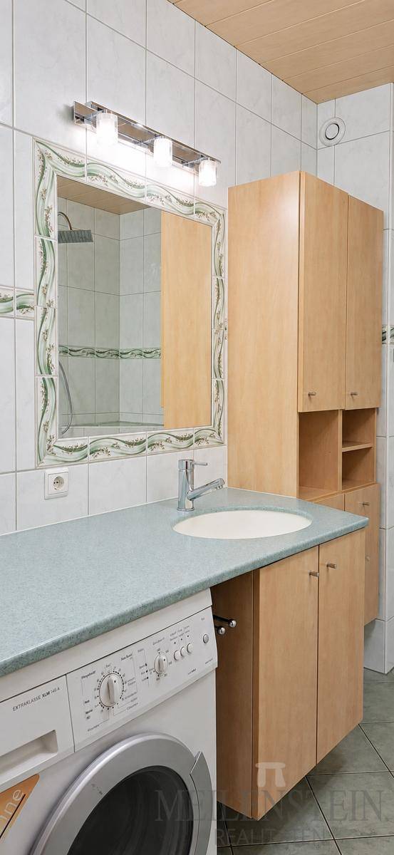 Badezimmer mit Einzelwaschbecken, Spiegelschrank, Holzmöbeln und integrierter Waschmaschine.