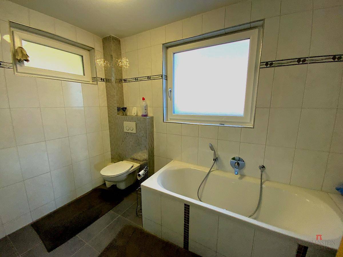 Gefliestes Badezimmer mit Badewanne, Toilette und Fenster für Tageslicht.