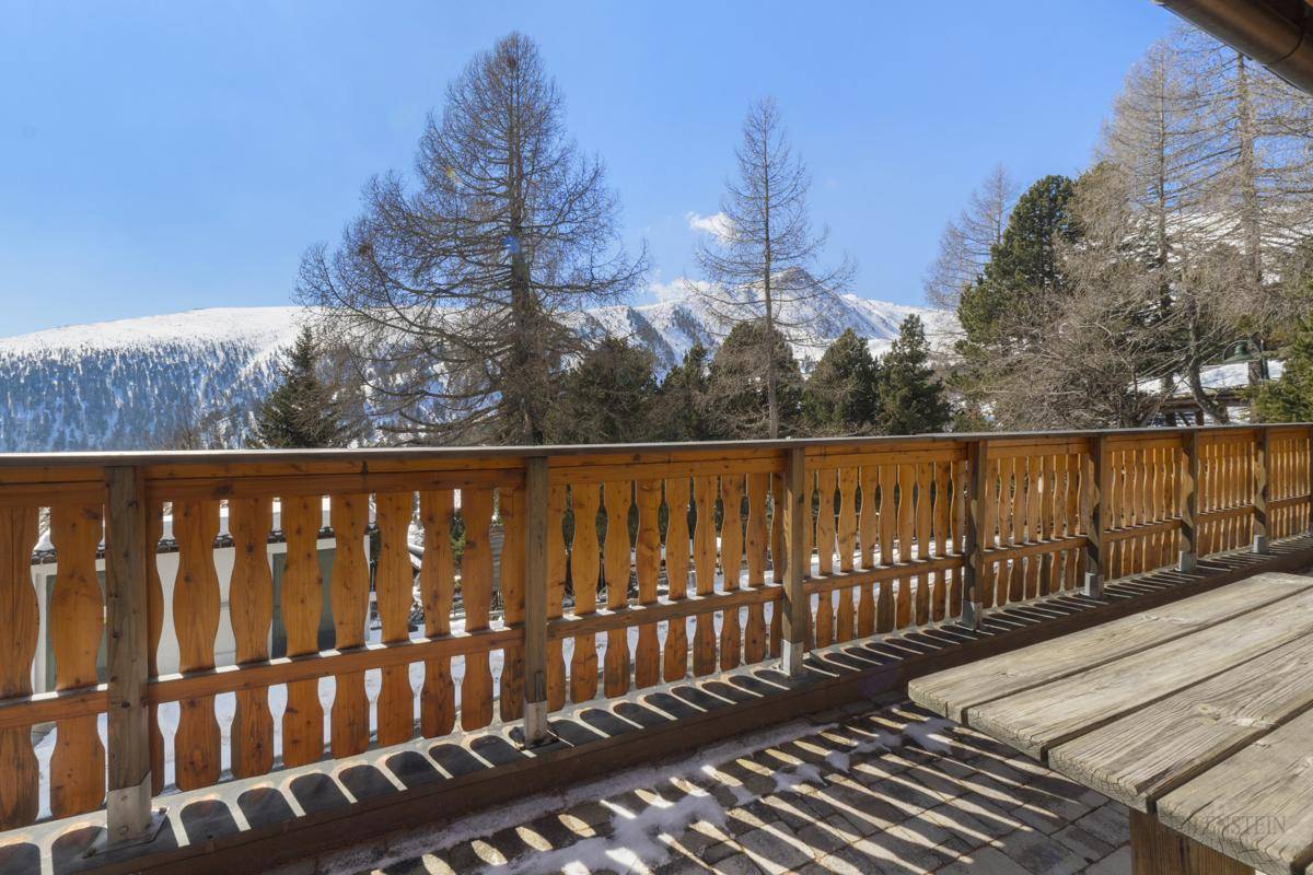 Balkon mit rustikalem Holztisch und weitem Blick auf die schneebedeckten Berge.