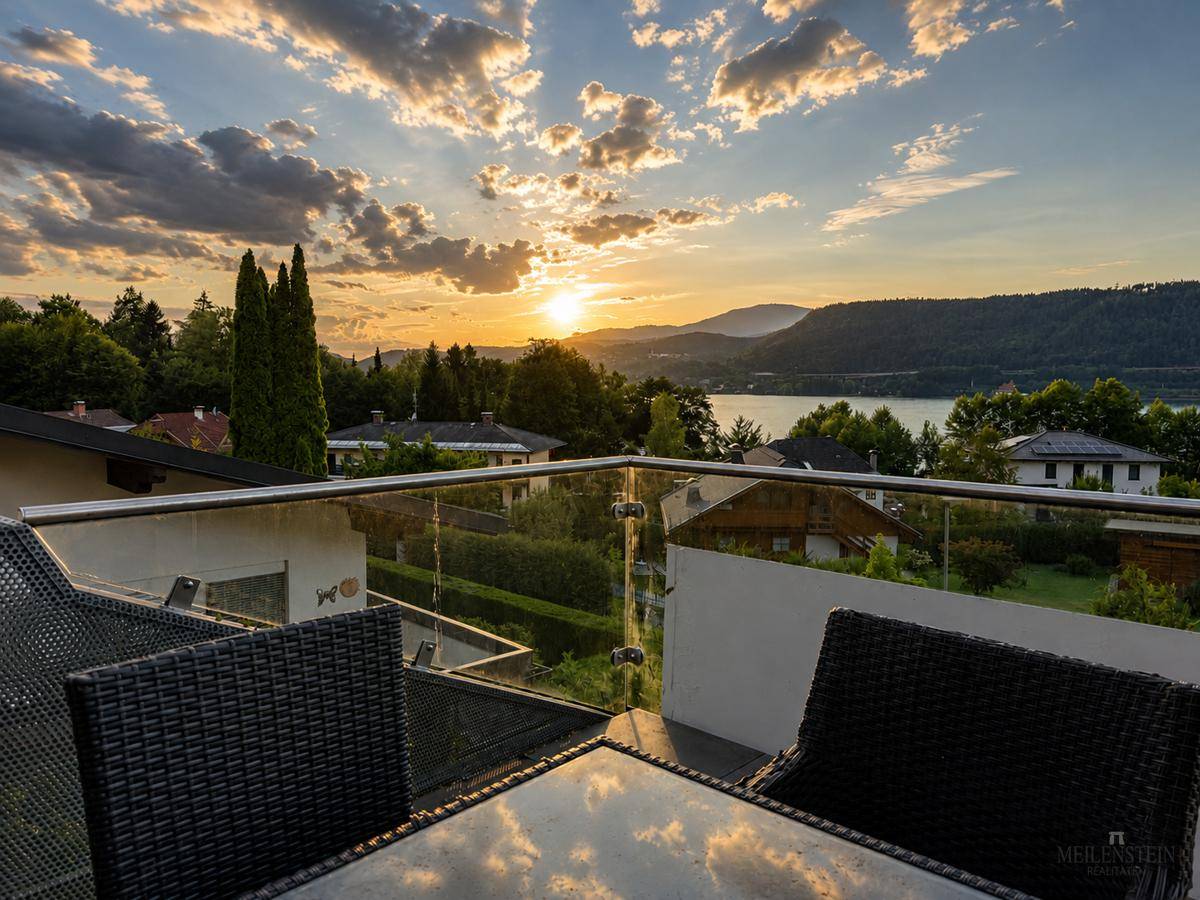 Gemütliche Terrasse mit Rattanmöbeln und Glasgeländer, ideal für entspannte Stunden mit Seeblick.