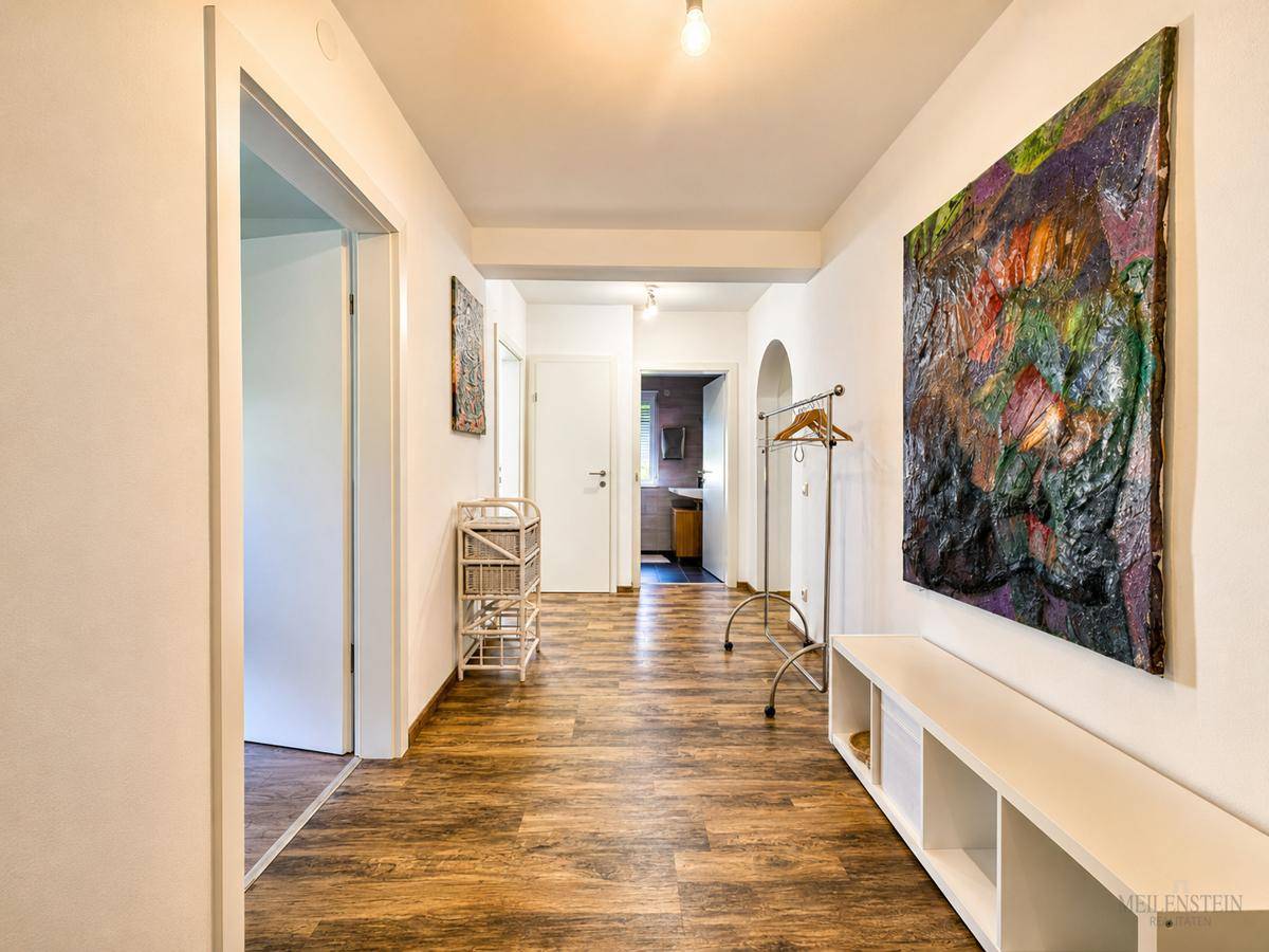 Geräumiger Flur mit Holzboden, Garderobe und einem großen, farbenfrohen Kunstwerk an der Wand.