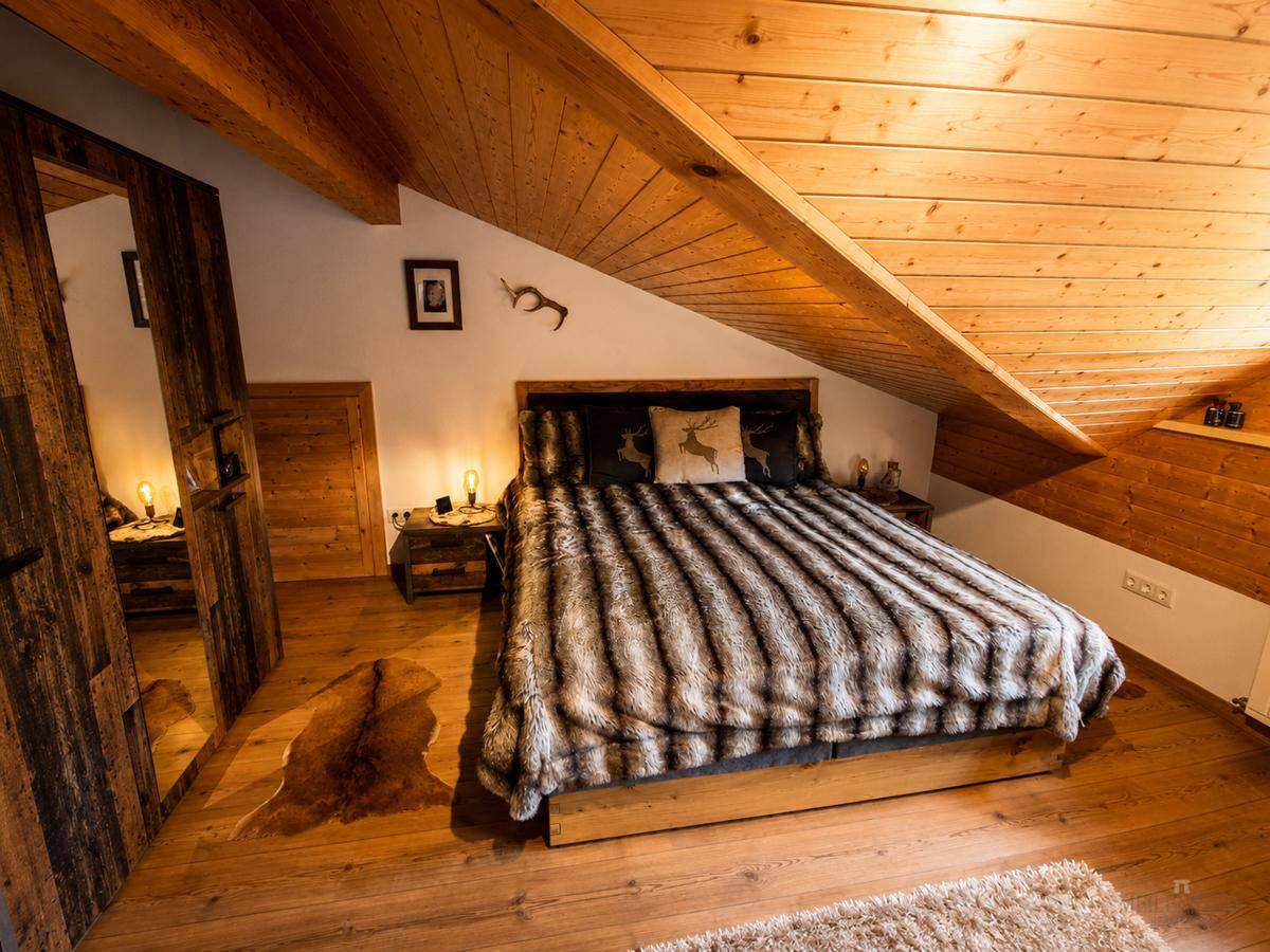 Rustikales Schlafzimmer im Dachgeschoss mit Holzwänden, Holzboden und einem großen Doppelbett.