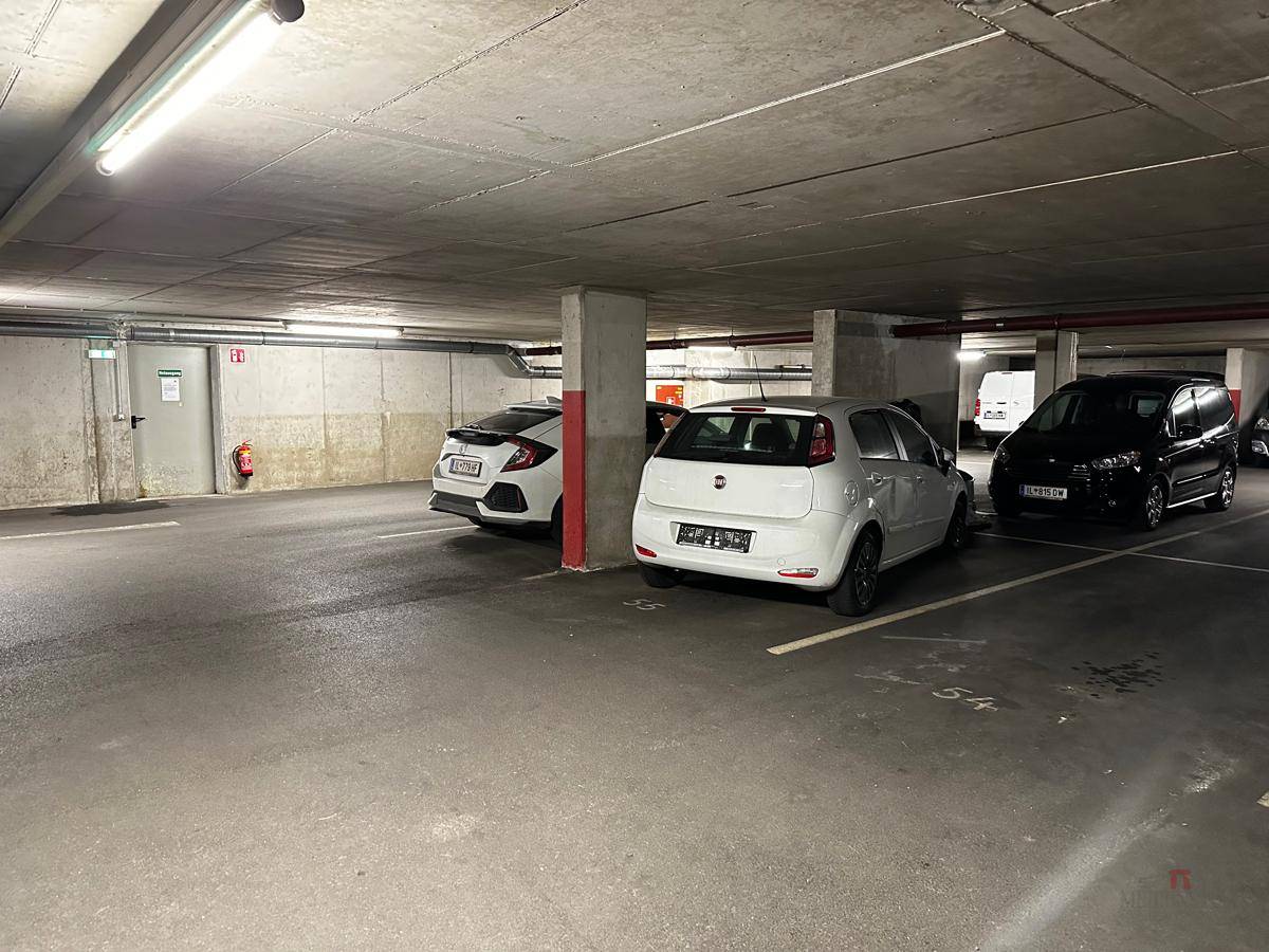 Weitere Ansicht der Tiefgarage mit geparkten Fahrzeugen, Betonpfeilern und einem Ausgangsschild.