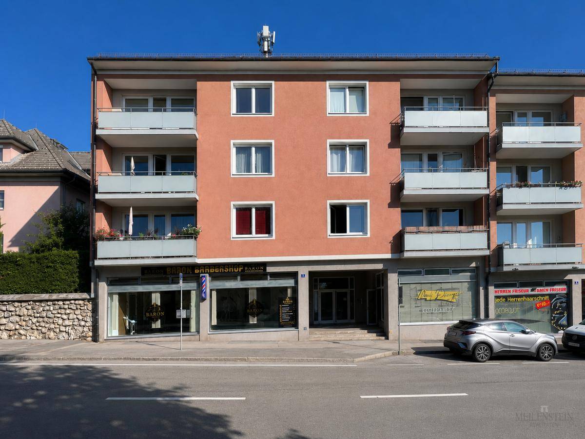 Vorderansicht des Wohngebäudes mit orangefarbener Fassade, Geschäften im Erdgeschoss und Balkonen.