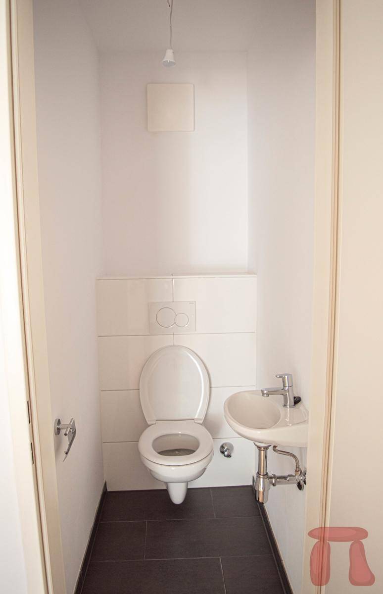 Gäste-WC mit wandmontierter Toilette, kleinem Waschbecken und Fliesenboden.