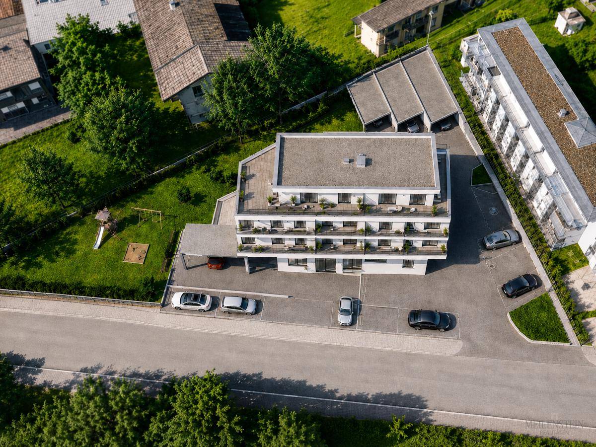 Luftaufnahme eines modernen Mehrfamilienhauses mit Flachdach, Parkplätzen und Grünflächen inklusive Spielplatz.