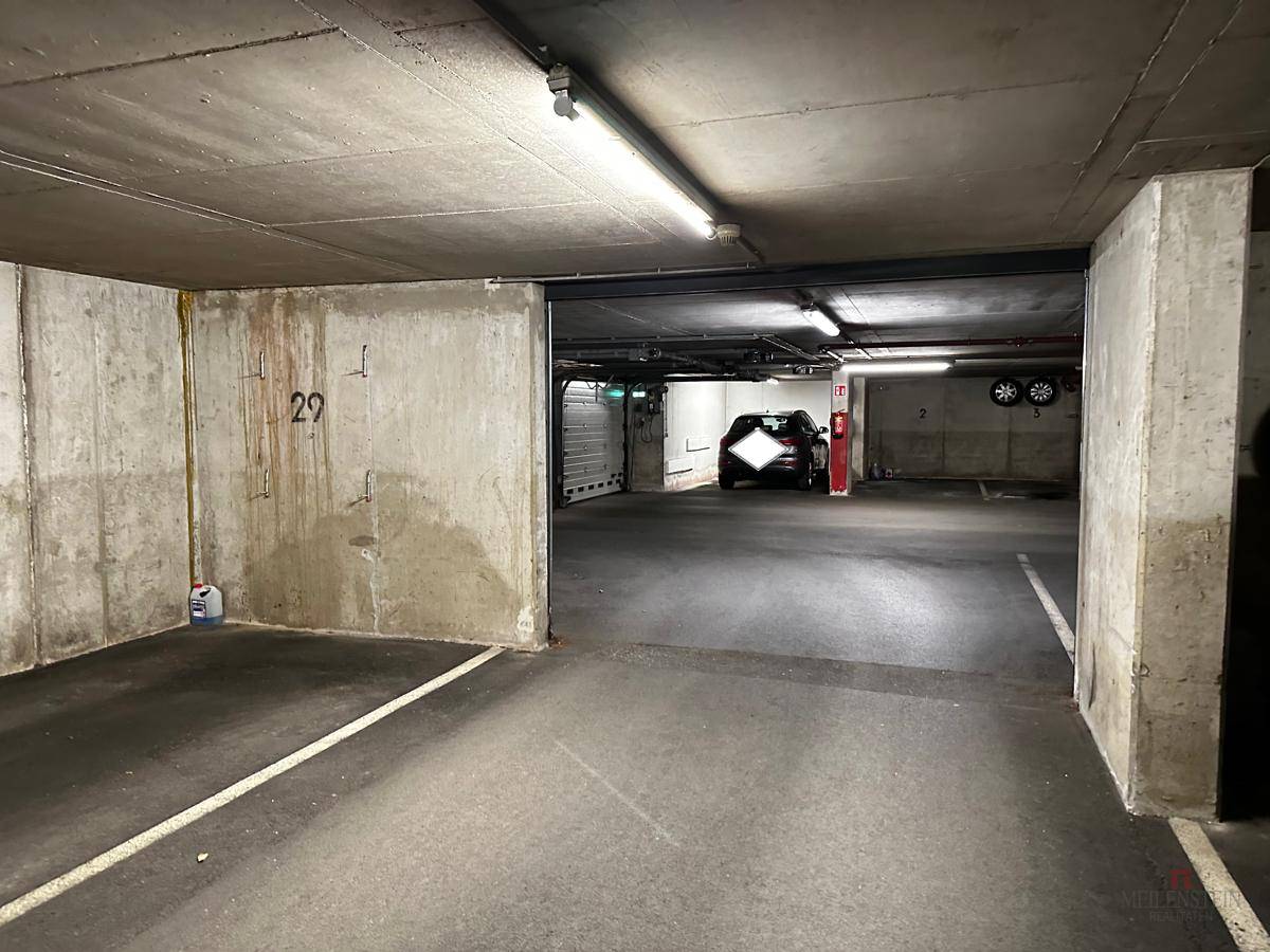 Geräumige Tiefgarage mit markierten Parkplätzen und Betonwänden, ein Fahrzeug ist im Hintergrund sichtbar.