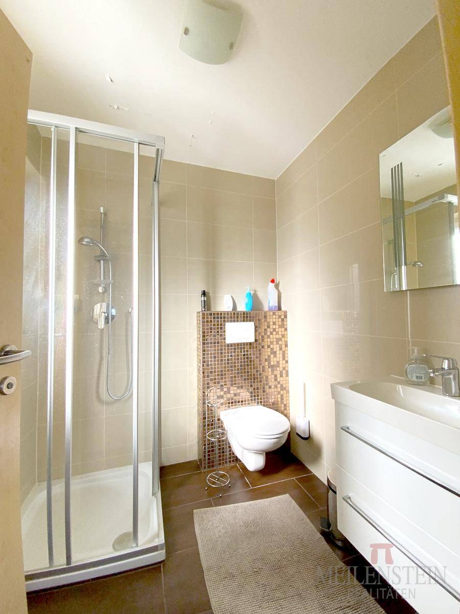 Modern gefliestes Badezimmer mit Duschkabine, wandhängendem WC und Einzelwaschbecken.