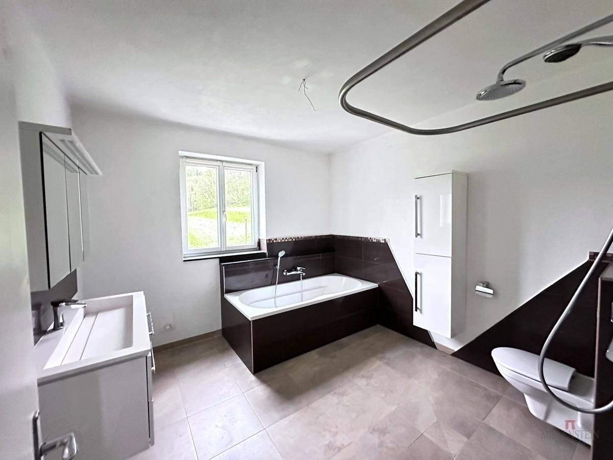 Helles Badezimmer mit Badewanne, modernem Waschtisch und Fenster mit Blick ins Grüne.