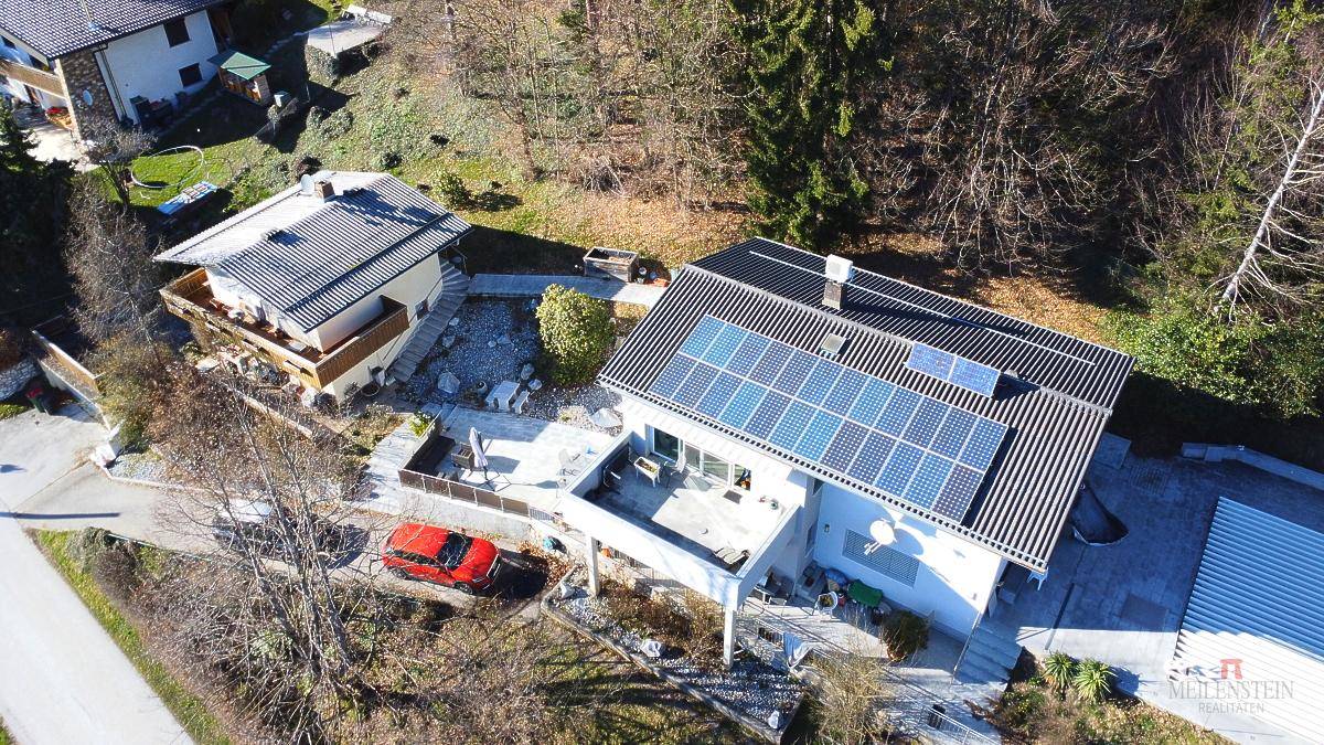 Luftaufnahme eines Hauses mit Solaranlage auf dem Dach und umliegender Natur.