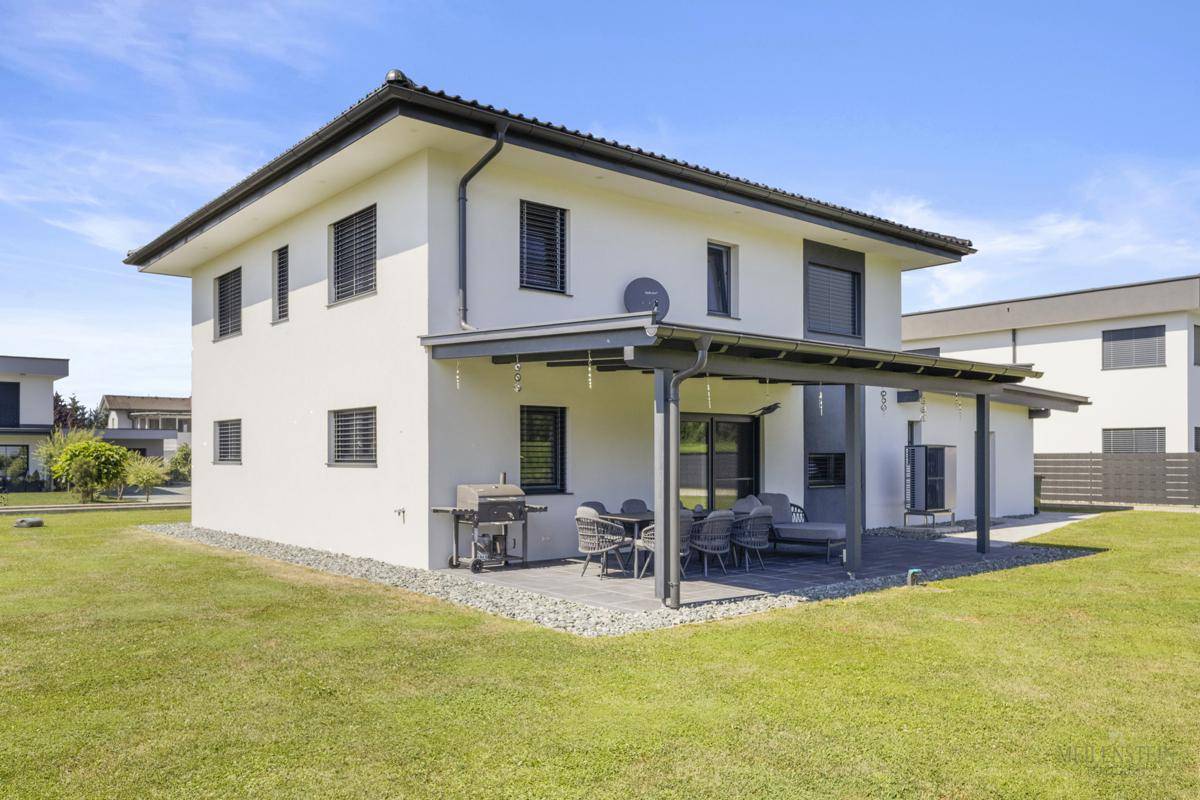 Überdachte Terrasse mit Gartenmöbeln und Grillbereich, umgeben von einem gepflegten Rasen.