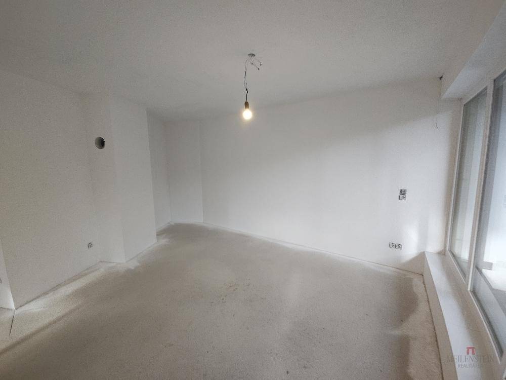 Helles, unfertiges Zimmer mit großen Fenstern und Rohbetonboden.