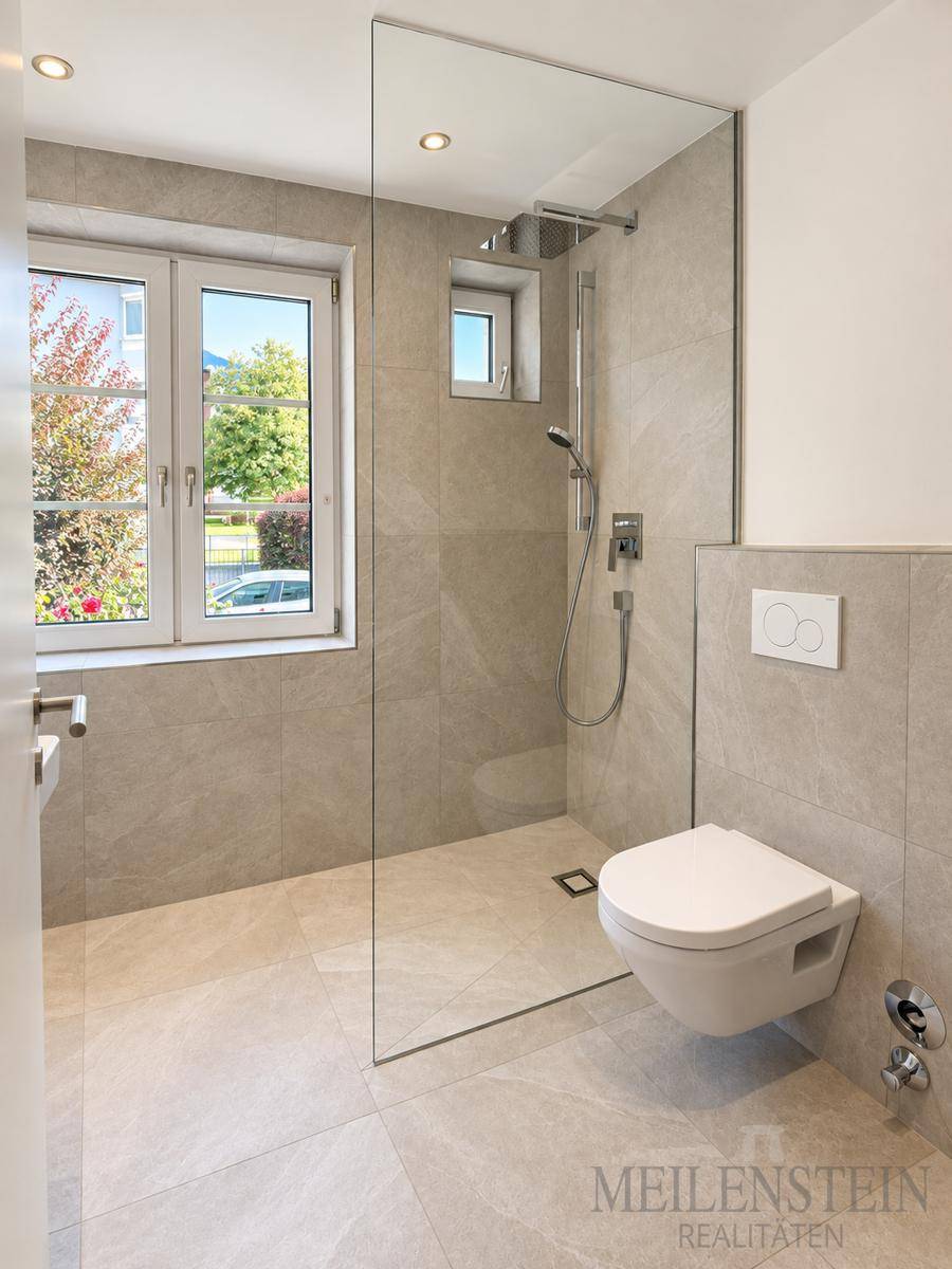 Helles Badezimmer mit bodengleicher Dusche, wandhängendem WC und Fenster.