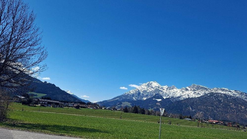 Weitläufige Landschaft mit grünen Wiesen und schneebedeckten Bergen unter blauem Himmel.