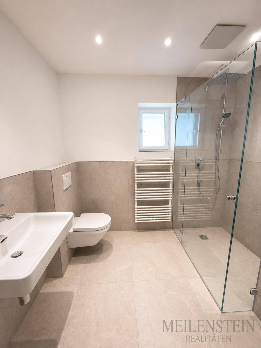 Modernes Badezimmer mit ebenerdiger Dusche, WC, Waschbecken und beheiztem Handtuchhalter.