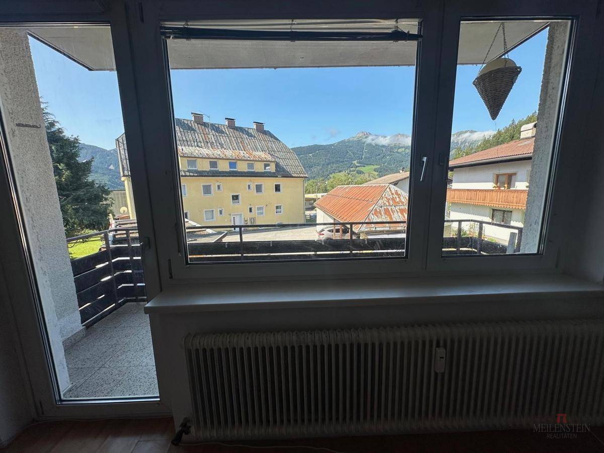 Blick aus einem Zimmer auf den Balkon mit Bergsicht und umliegenden Häusern.