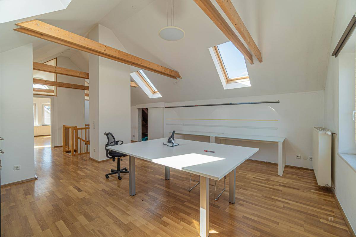 Geräumiger Dachgeschossraum mit Holzboden, freiliegenden Holzbalken und mehreren Dachfenstern für viel Licht.