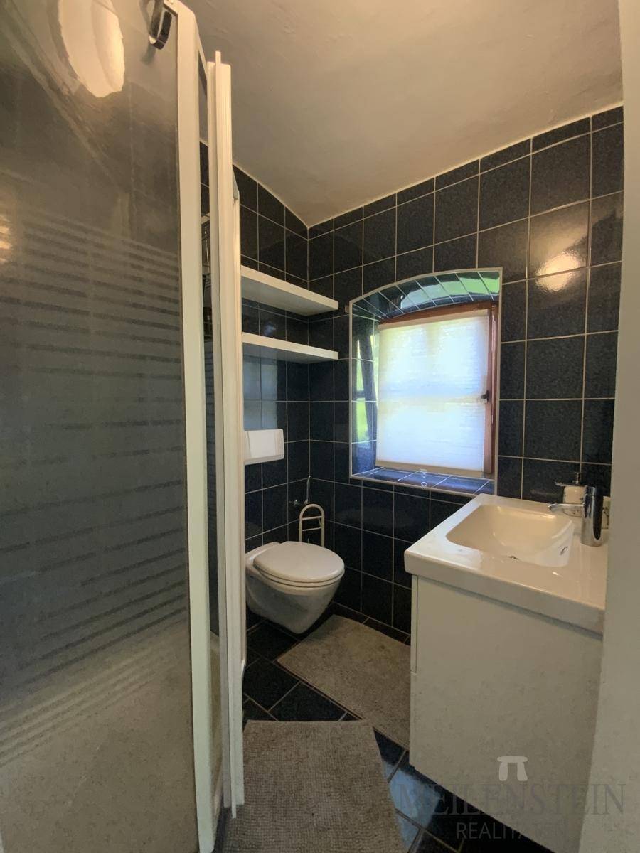 Funktionales Badezimmer mit dunklen Fliesen, einer Duschkabine, WC, Waschbecken und einem kleinen Fenster.