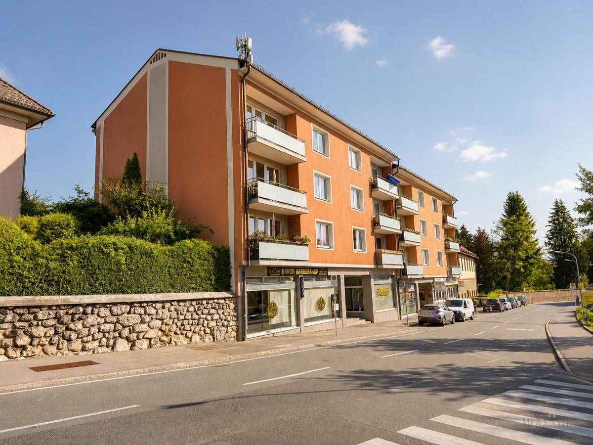 Ansicht des orangefarbenen Mehrfamilienhauses mit Geschäften im Erdgeschoss und Balkonen.