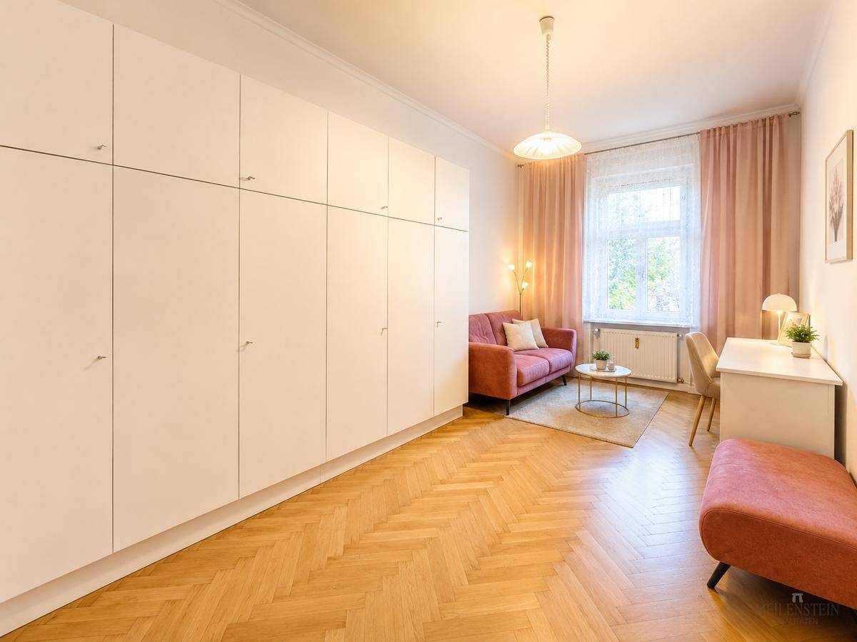 Helles Zimmer mit großem Einbauschrank, rosa Sofa und Schreibtisch.