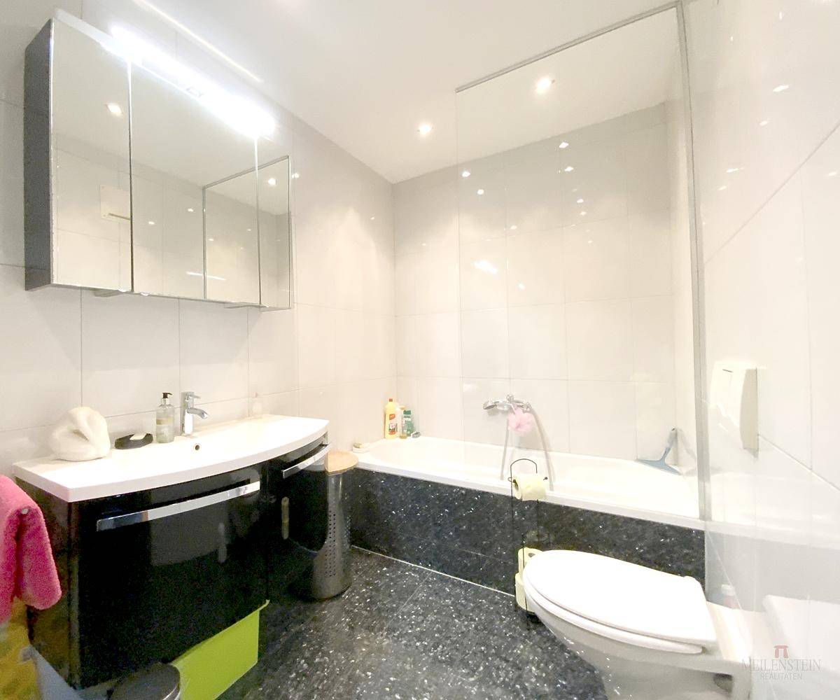 Modernes Badezimmer mit Badewanne, Waschtisch und Spiegelschrank in Schwarz-Weiß-Fliesen.