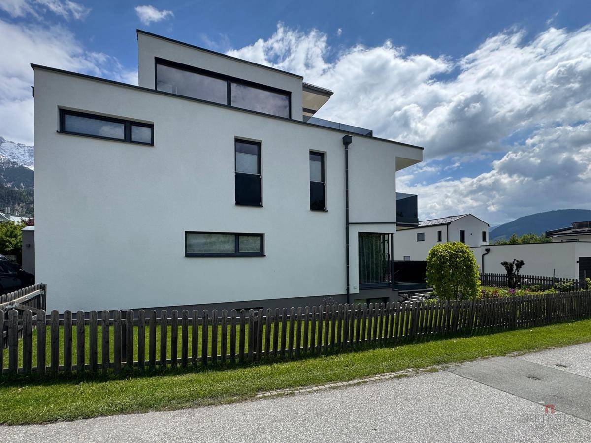 Moderne weiße Fassade des Gebäudes mit klaren Linien und einem Holzzaun im Vordergrund.