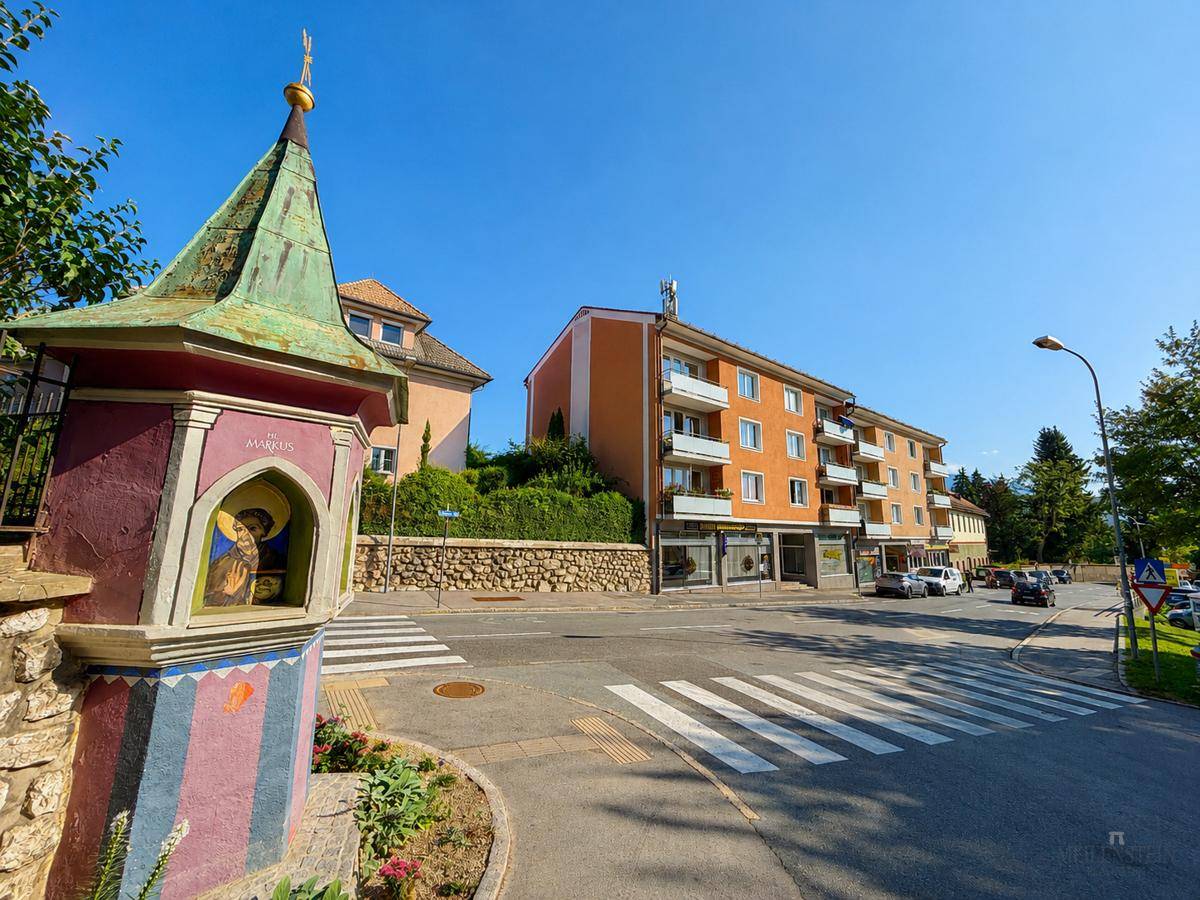 Straßenansicht mit einem kleinen Schrein, Zebrastreifen und einem orangefarbenen Mehrfamilienhaus.