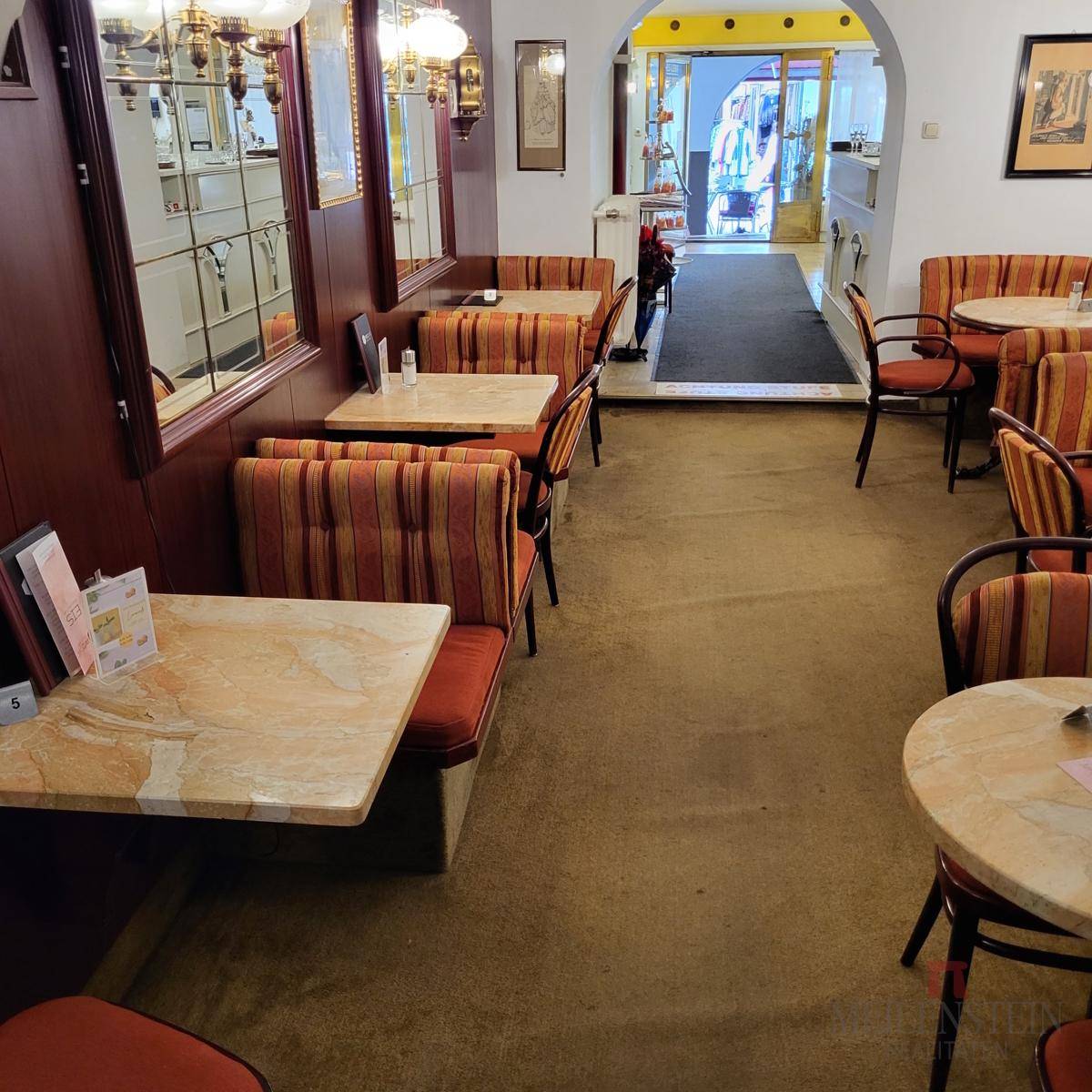 Gemütlicher Café-Sitzbereich mit gepolsterten Bänken, kleinen Tischen und Blick zum Eingangsbereich.