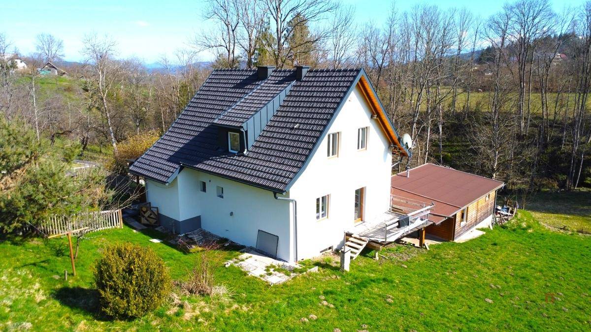 Seitenansicht des Hauses aus der Luft mit einem Anbau und Treppen, umgeben von grünen Wiesen.