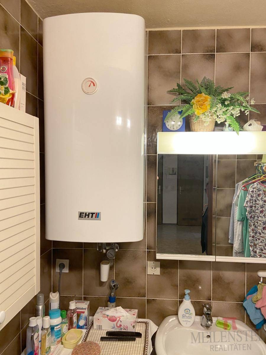 Badezimmer mit Warmwasserboiler, Waschbecken und Spiegelschrank, funktional eingerichtet für den täglichen Gebrauch.