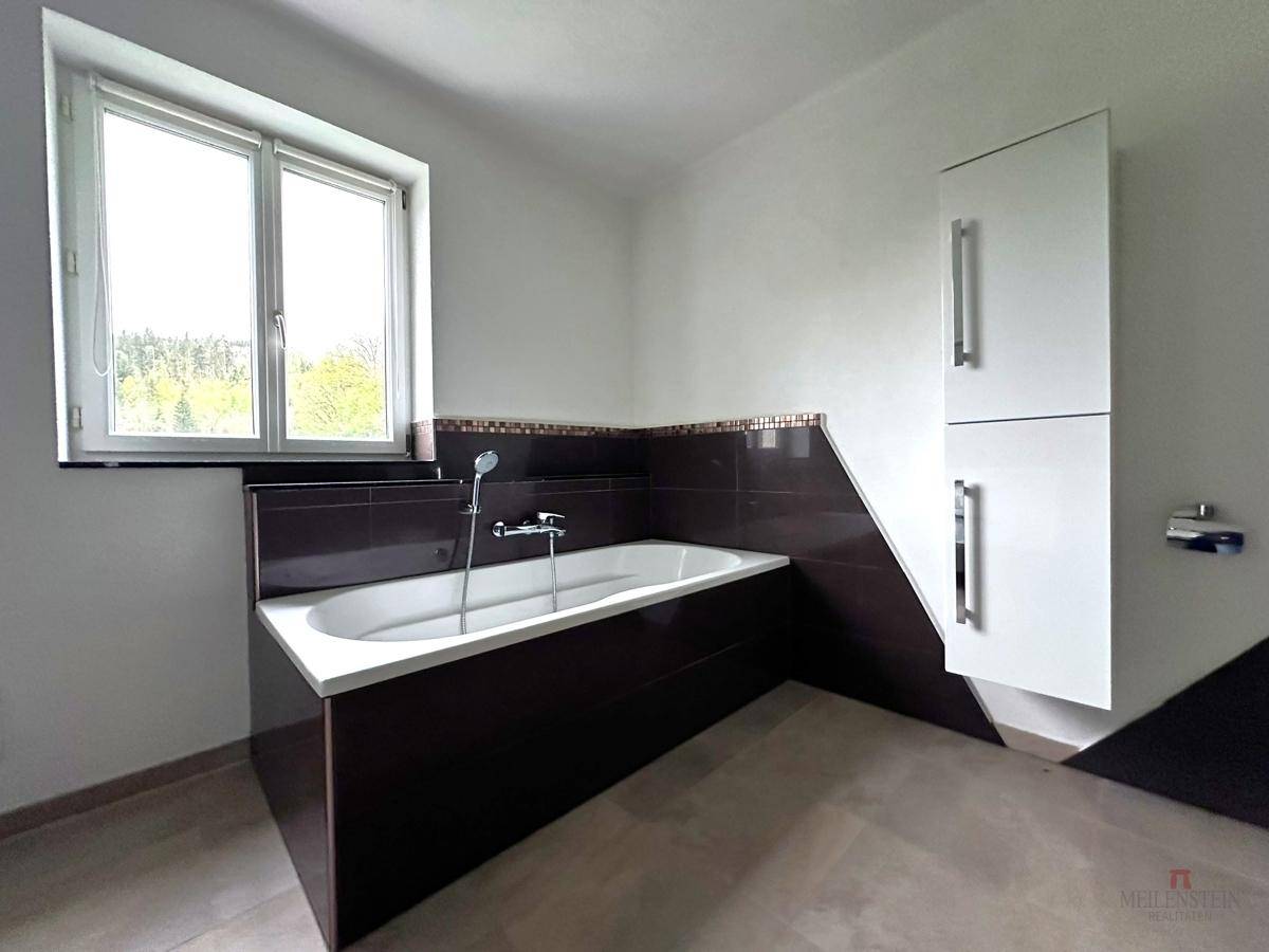 Detailansicht des Badezimmers mit Badewanne, dunklen Fliesen und einem großen Fenster.