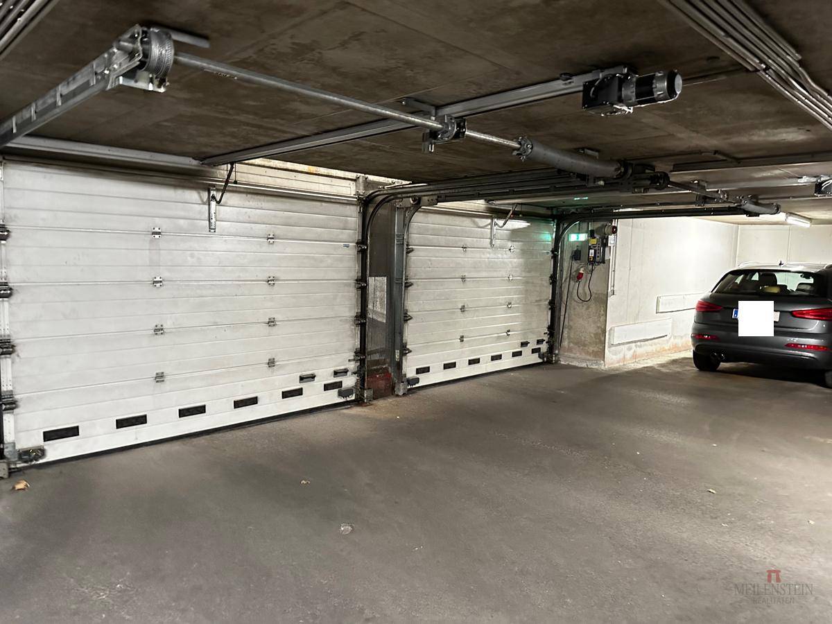 Innenansicht der Tiefgarage mit zwei weißen Garagentoren und einem geparkten Fahrzeug.