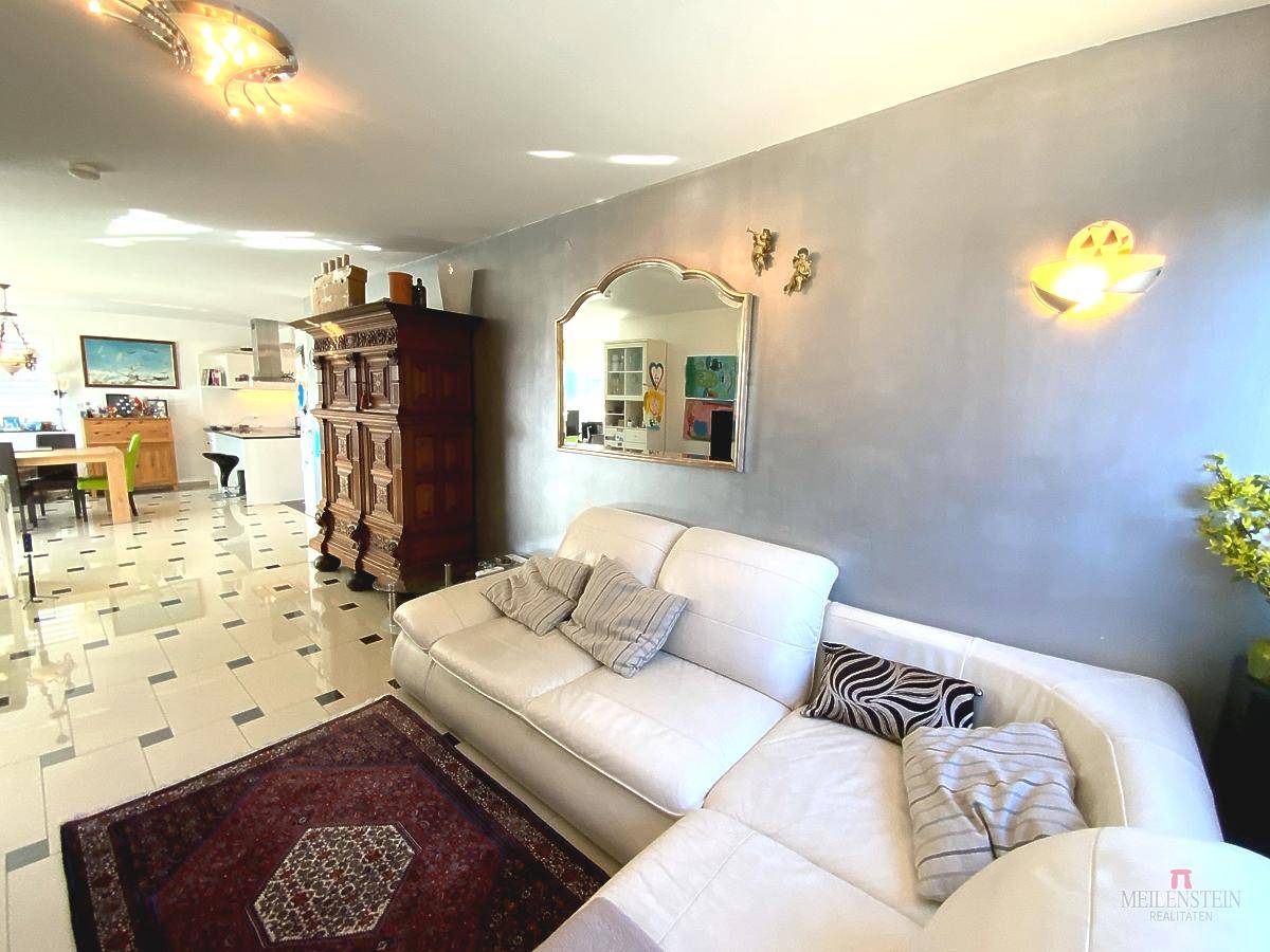 Gemütliches Wohnzimmer mit weißem Ecksofa, Teppich und Blick in den Essbereich.