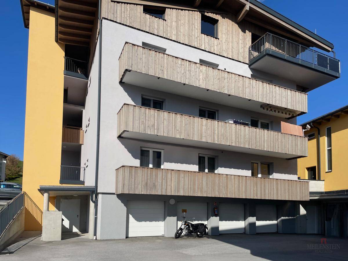 Seitenansicht eines modernen Wohngebäudes mit Holzverkleidung, Balkonen und Garagen im Erdgeschoss.