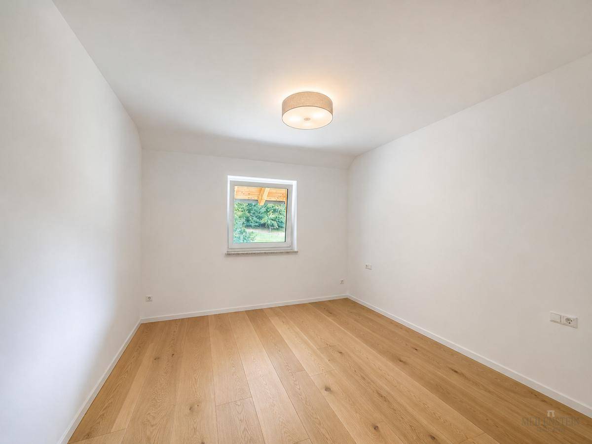 Helles, leeres Zimmer mit Holzboden und weiß gestrichenen Wänden, ideal als Schlaf- oder Gästezimmer.