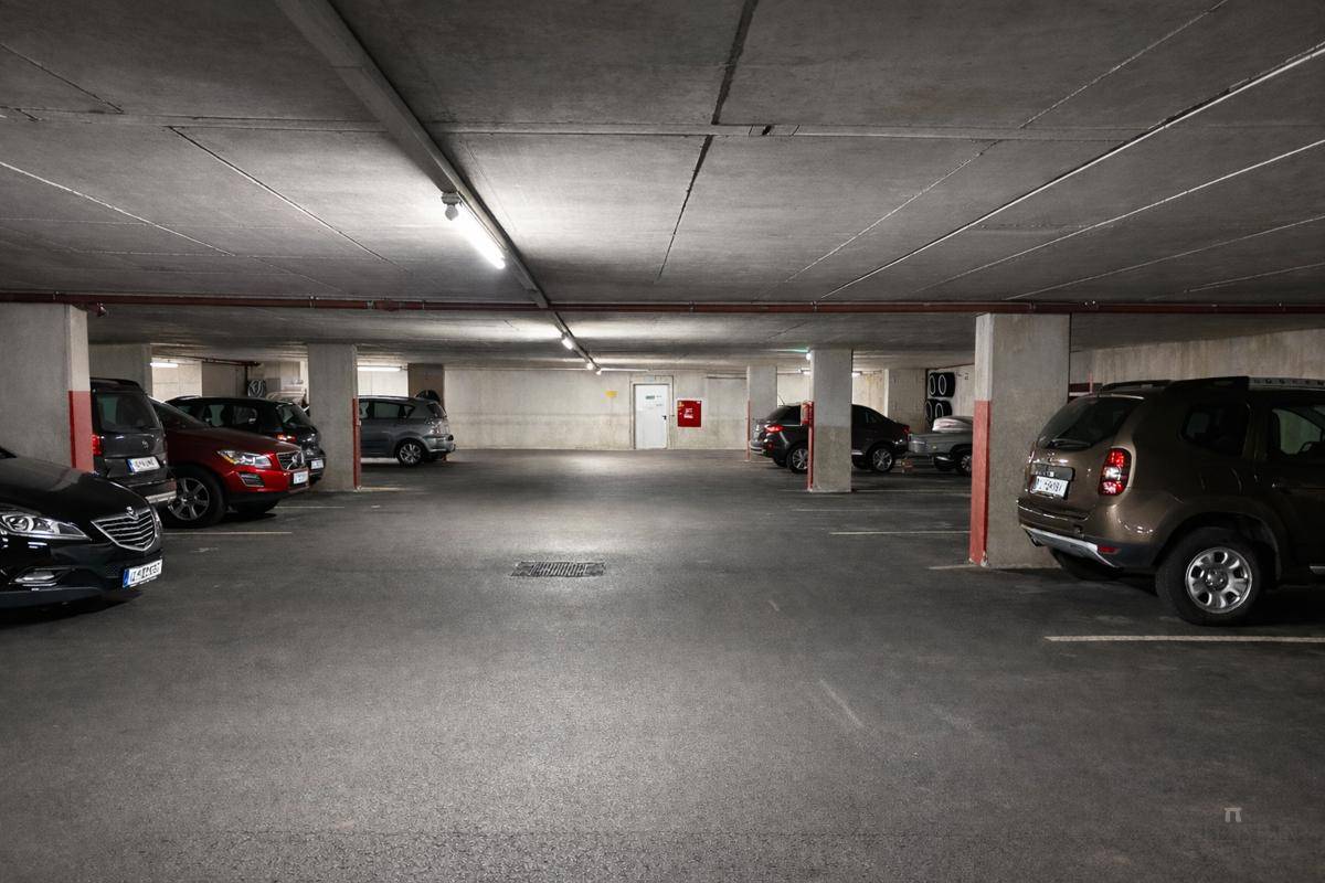 Weitläufige Tiefgarage mit vielen Stellplätzen, Säulen und Deckenbeleuchtung, gut beleuchtet.