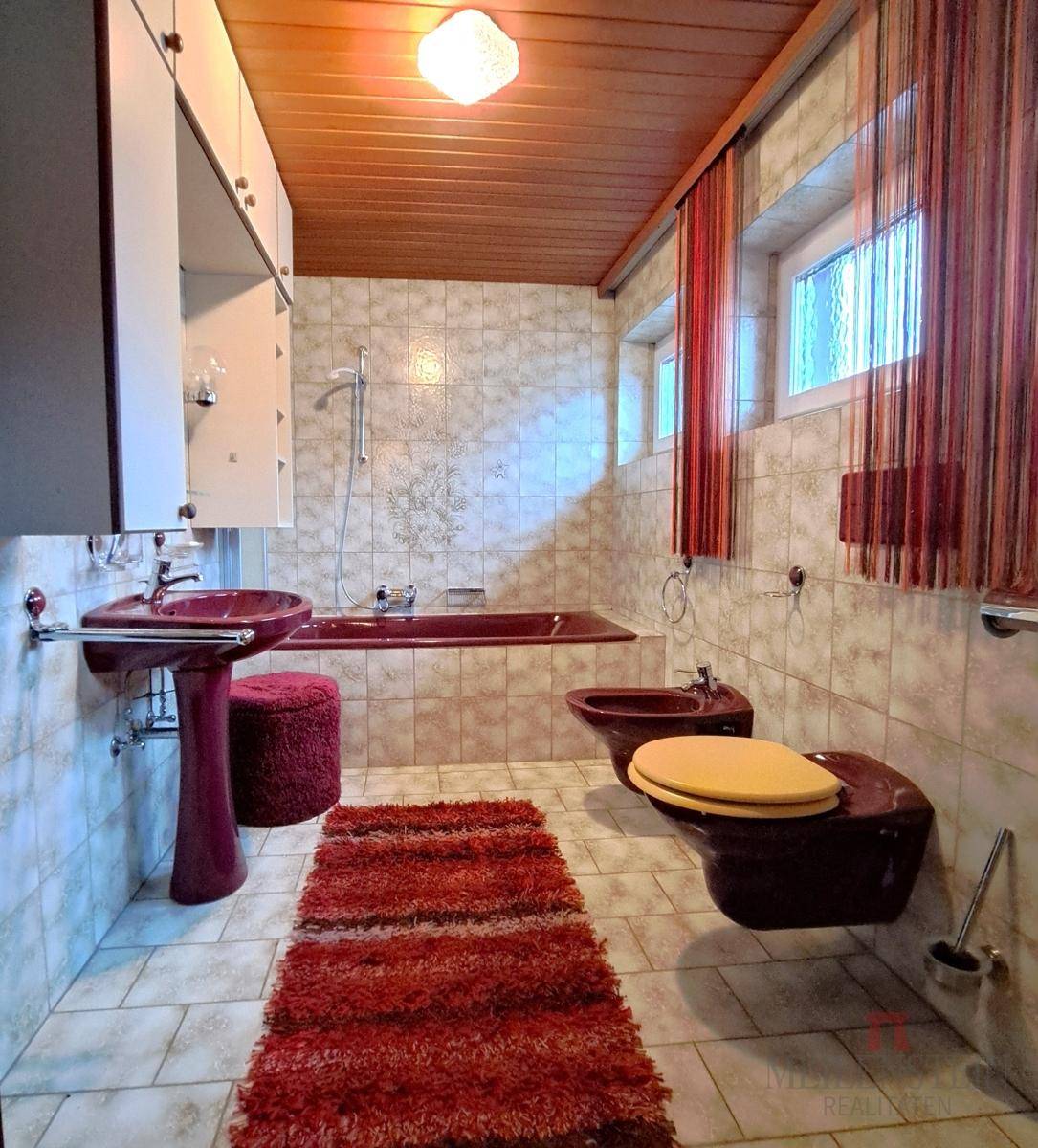 Badezimmer im 80er-Jahre-Stil mit roter Badewanne, Bidet und hellen Fliesen.