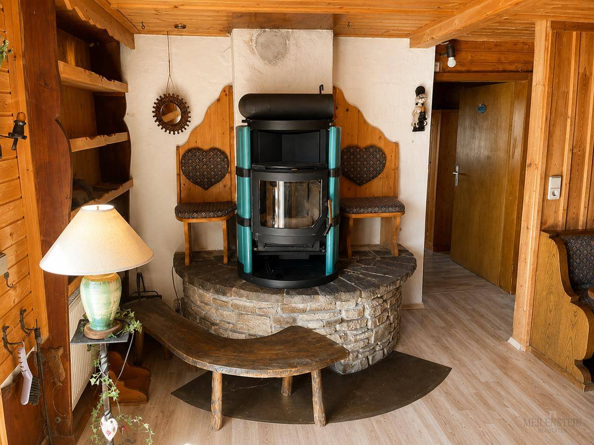 Wohnzimmer im alpinen Stil mit Kaminofen auf Steinsockel und Holztäfelung.