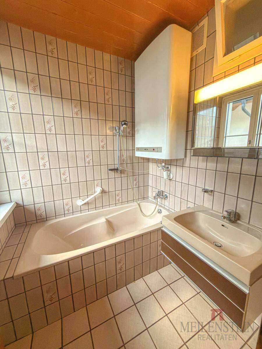 Badezimmer mit Badewanne, Waschbecken und Fliesen im 80er-Jahre-Stil.