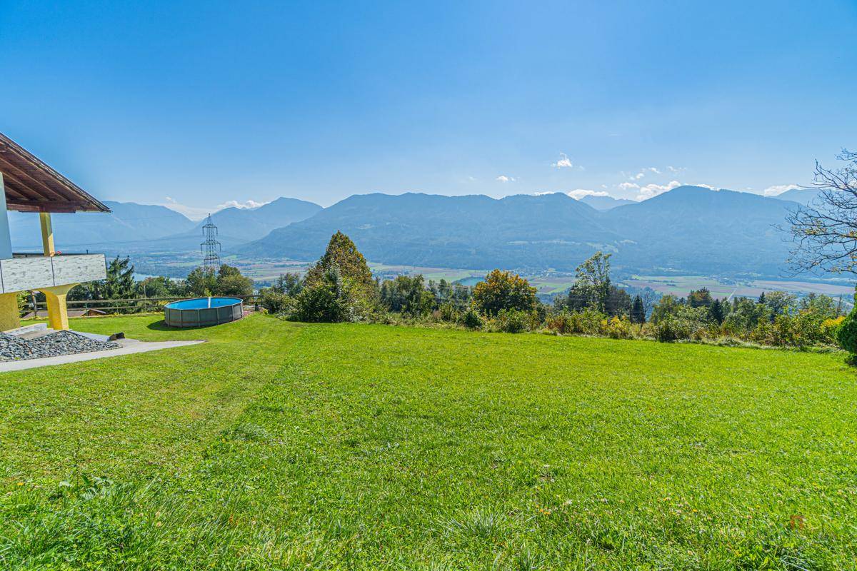 Grüne Wiese vor einem Haus mit Terrasse und weitem Blick über das Tal und die Berge.