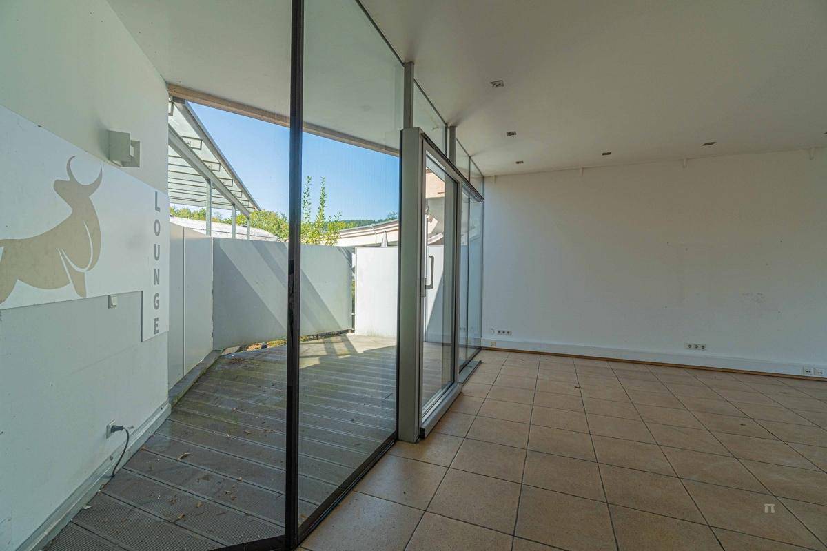 Heller Innenraum mit Fliesenboden und Zugang zu einer Holzterrasse durch große Glasfronten.